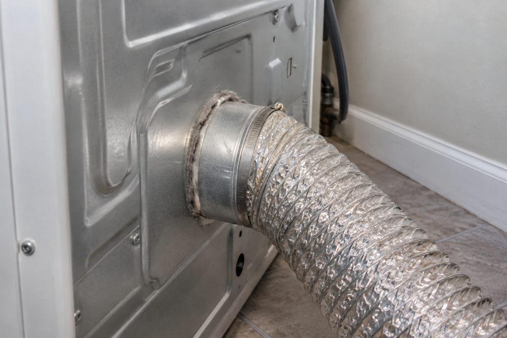 Close-up of a dryer's rear vent port with a corrugated exhaust hose and visible lint.